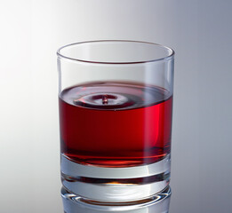 Drop dripping on wine surface in glass close up view. Red wine drop with concentric waves.