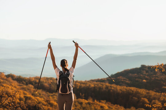 Woman Happy To Hike Top Of Mountain And Hold Trekking Poles. Nordic Walking Outdoors, View From Behind. Travel Lifestyle. Success Goal Achievement.