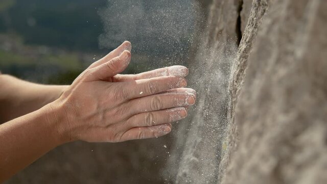 SLOW MOTION, CLOSE UP, DOF: Unrecognizable climber claps her hands to get rid of excess magnesium before continuing her ascent. Woman top rope climbing chalks up her hands midway during her climb