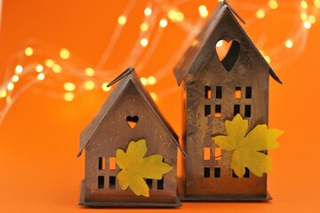 Autumn time. Thanksgiving Day.Small houses lanterns and autumn yellow maple leaves on a  orange background with shining garlands. Fall time symbol.Autumn mood