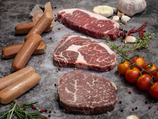 top view of various cuts of raw meat steak with herbs on grey concrete background. food preparation concept.