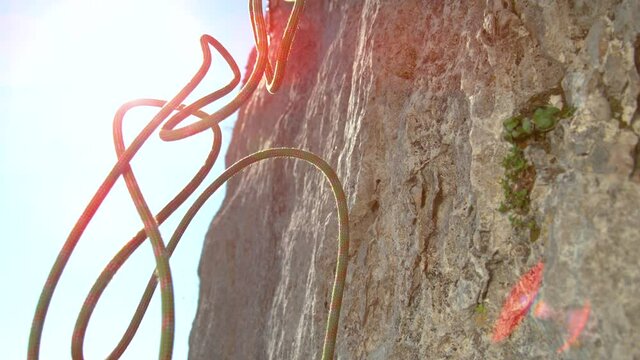 SLOW MOTION, CLOSE UP, LENS FLARE, DOF: Green and red rope falls from the top of a cliff on a sunny summer day. Safety rope gets released after a group of rock climbers all reach the top of rocky wall