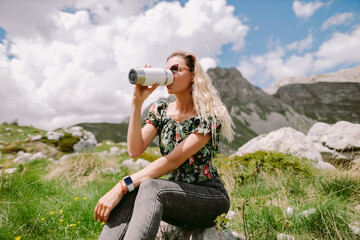 pretty woman drinking coffee with mug and relax in mountains. Attractive woman holding tea mug and travel in mountains with beautiful summer view. National park of Durmitor, Montenegro. 