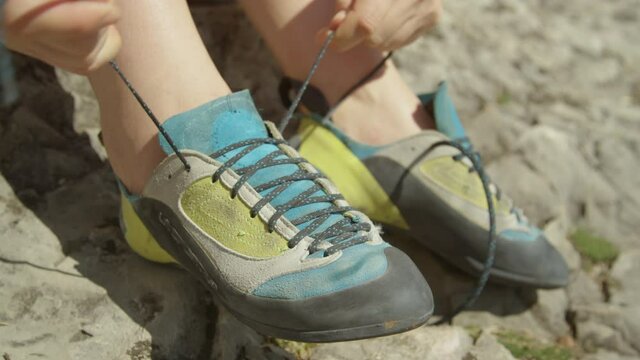 SLOW MOTION, CLOSE UP, DOF: Athletic woman on rock climbing trip gets ready for her first ascent by tying her shoes. Unrecognizable woman ties her climbing shoes before climbing a difficult boulder.