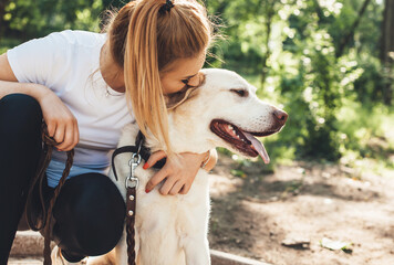 Close up photo of a caucasian woman and her golden retriever embracing in the park in a sunny summer day