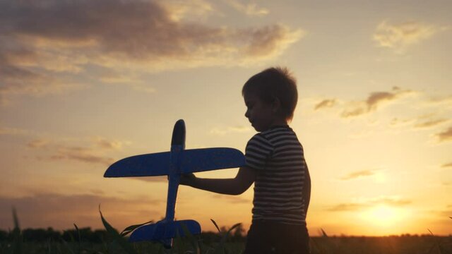 happy boy child runs with an airplane. kid silhouette play aircraft. happy family dream freedom concept. son runs on a wheat field at lifestyle sunset holds in his hands toy plane