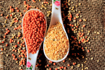 Pile of uncooked red lentils and pigeon pea. Mung beans and red lentils in two spoons isolated on sack textured background.