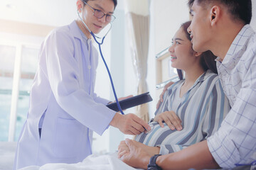 Doctor using stethoscope for examining pregnant woman with her husband at hospital