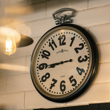 Hanging on the white wall vintage classic clock and copper lamp in a French coffee shop. Inscription on the watch "Paris"
