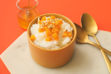 Bowl with boiled rice and pumpkin on color background