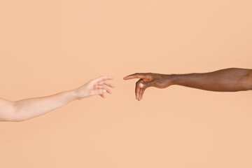 Hands of Caucasian woman and African-American man reaching out to each other on color background....