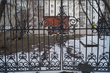 Photo of an iron grating against the background of a poor quarter and outbuildings.