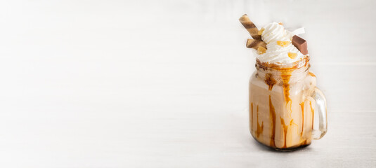 Milkshake mason jar with whipped cream and caramel decorated with candied fruit  and wafer rolls on white background. Large background for banner with copy space.