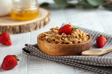 Homemade granola in a wooden bowl with strawberries and honey on wooden background. The concept of a healthy Breakfast.
