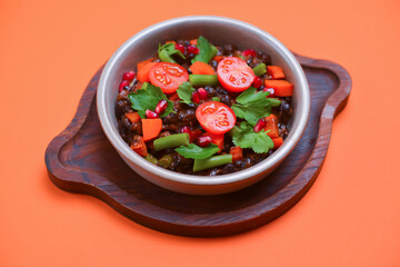 Stew of chicken meat with vegetables and pomegranate seeds served in a bowl over bright orange background.