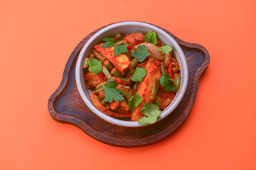 Stew of chicken meat with vegetables and pomegranate seeds served in a bowl over bright orange background.