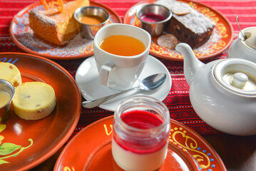 Table set for tea time with sweet desserts. Chocolate brownie cake, vanilla cake, panna cotta. Tea pot with sweet tea.
