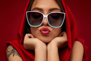 Portrait of beautiful brunette sexy girl with luxurious make-up in white sunglasses and red headscarf on red background