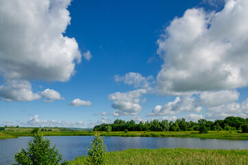 Big white clouds float over a lake in a forest against a blue sky, nature traveling on isolation. Nature.