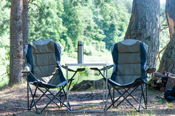 Theme of hiking and tourism, a symbolic landscape, two empty camping chairs and picnic  table are...