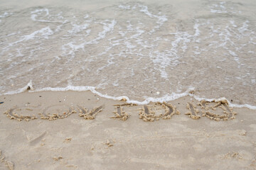 Words COVID-19 on the sand and the beach  is clean by wave  , Coronavirus pandemic. An outbreak on vacation. Traveling cancelled concept.