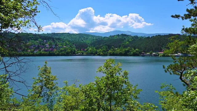 Beautiful and sunny lake view with trees, hills, houses,mountains, by the water.