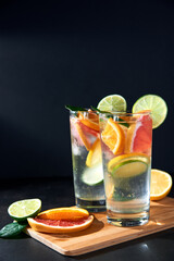 Health care, fitness, healthy nutrition diet concept. Fresh cool homemade citrus infused detox water with grapefruit, orange, lemon and lime and ice in glasses on dark background.