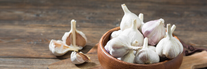 Garlic in a wooden bowl on a wooden table. lots of garlic in a bowl. Garlic close-up. Banner with space for text