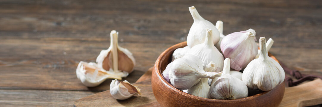Garlic in a wooden bowl on a wooden table. lots of garlic in a bowl. Garlic close-up. Banner with space for text