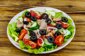 Tasty tuna salad with lettuce, black olives and fresh vegetables on wooden table