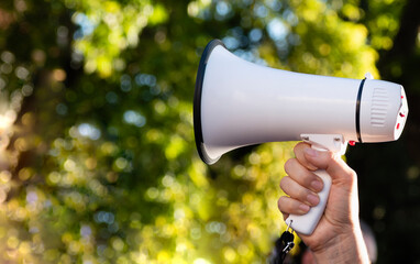 Megaphone in female hand on natural blurred background of greenery in the park. Concept of protest...