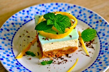 Cheesecake slice. Slice of cheesecake on blue plate. Homemade cheesecake piece with lemon & mint for dessert. Healthy mascarpone cheese cake piece dessert. Slice citron cake with pudding. Cake closeup
