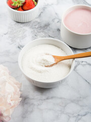 Collagen protein powder in bowl with wooden spoon on marble table. Adding collagen to strawberry yogurt