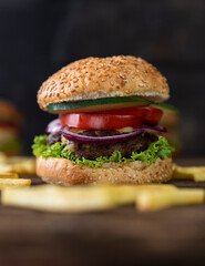 Hamburger with tomatoes, onions, cucumber, lettuce , melting cheese and french fries served on a  rustic wooden table