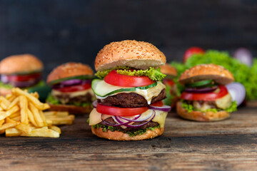 Double Hamburger with tomatoes, onions, cucumber, lettuce , melting cheese and french fries  served on a  rustic wooden table