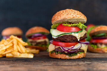 Double Hamburger with tomatoes, onions, cucumber, lettuce , melting cheese and french fries  served on a  rustic wooden table