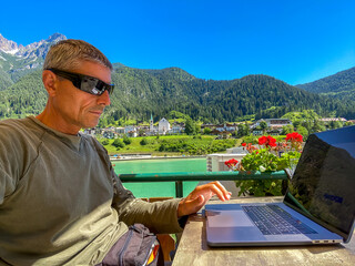 Relaxed man working with laptop in front of a mountain lake. Business and tourism concept