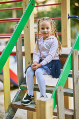 Little girl alone sits on the playground on the steps of the playhouse and laughs