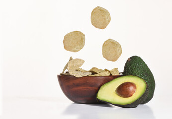 Crispy avocado chips on wooden bowl with fresh avocado fruit on white background, vegetarian concept, fast and quick food idea