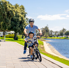Obraz premium Father and son riding their bikes having fun together in the park by the lake