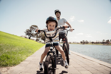 Father and son riding their bikes having fun together in the park by the lake