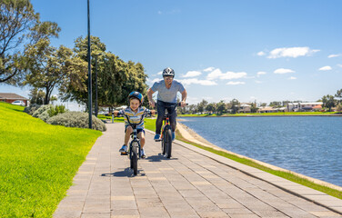 Obraz premium Father and son riding their bikes having fun together in the park by the lake