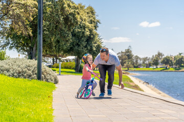 Fototapeta premium Father teaching his little daughter to ride a bike and having fun together at the park