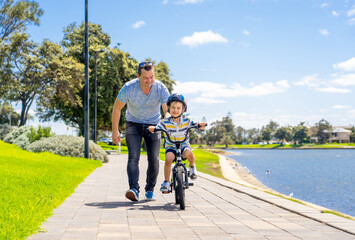 Obraz premium Father teaching his son to ride a bike and having fun together at the park