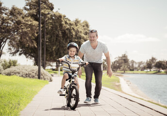 Obraz premium Father teaching his son to ride a bike and having fun together at the park