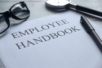 Selective focus of glasses,magnifying glass,pen and paper written with Employee Handbook on white wooden background.