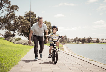 Father teaching his son to ride a bike and having fun together at the park
