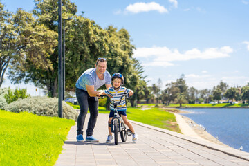 Obraz premium Father teaching his son to ride a bike and having fun together at the park