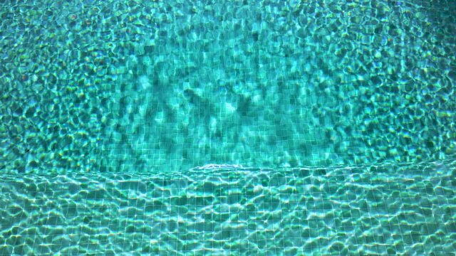 A game of glare on green water in the pool. Glare on the ripples on the background of the pixel tiles at the bottom interestingly refract the light. The edge of the pool resembles a mountain