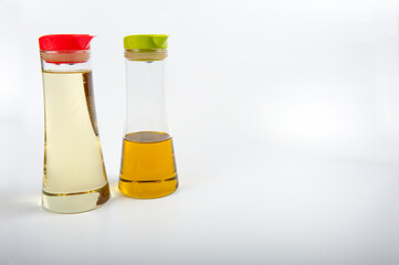 Two modern oil decanters with plastic lids. One lid is red and one is lime green.  The bottles contain olive oil and sunflower oil. The containers are placed in the left side of the image.